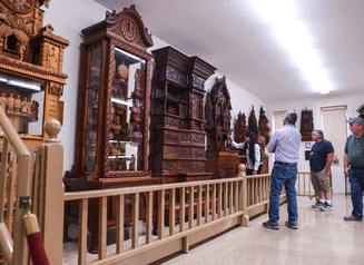 Several visitors gaze at a wall lined with wood clocks intricately carved by the Bily brothers