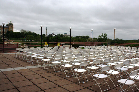 Many rows of chairs set up for a wedding ceremony on the Cafe Terrace of the State Historical Building with a view of the Iowa State Capitol building.