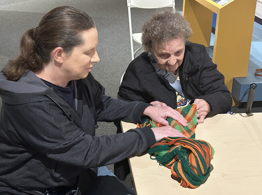Two museum visitors feel the texture of woven yarn in a sash made by Adeline Wanatee.